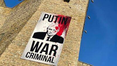 На стене Нарвского замка вывешен плакат "Путин - военный преступник"